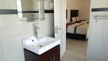 A hotel bathroom with a white sink, a glass shelf, and a mirror.