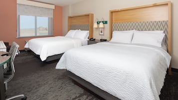 A hotel room with two beds, a desk, a chair, and a window.