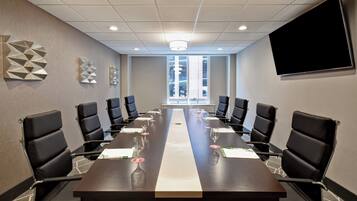 A conference room with a long table, black chairs, and a large screen on the wall.