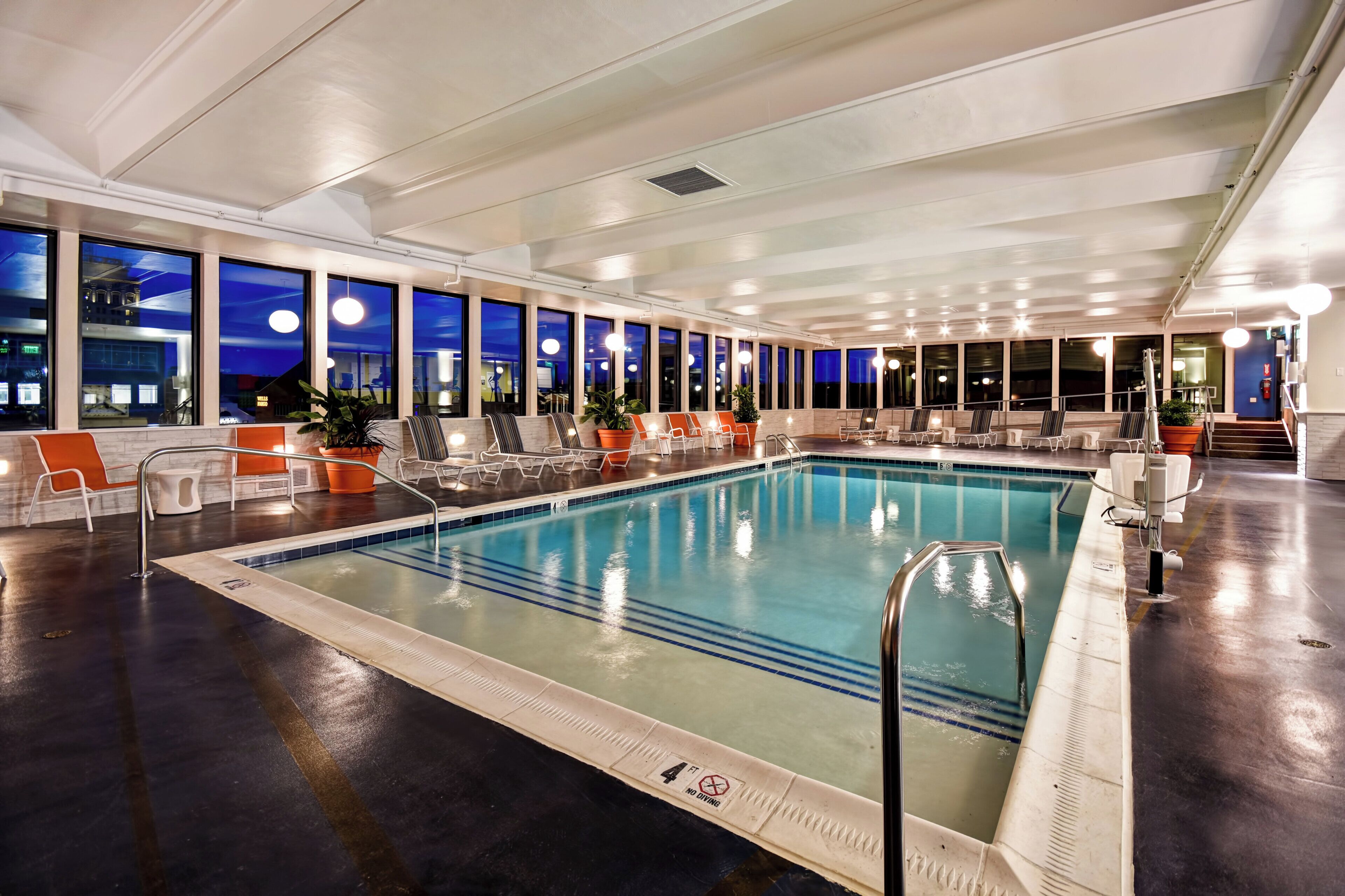 An indoor swimming pool with multiple lounge chairs and a view of the city at night.