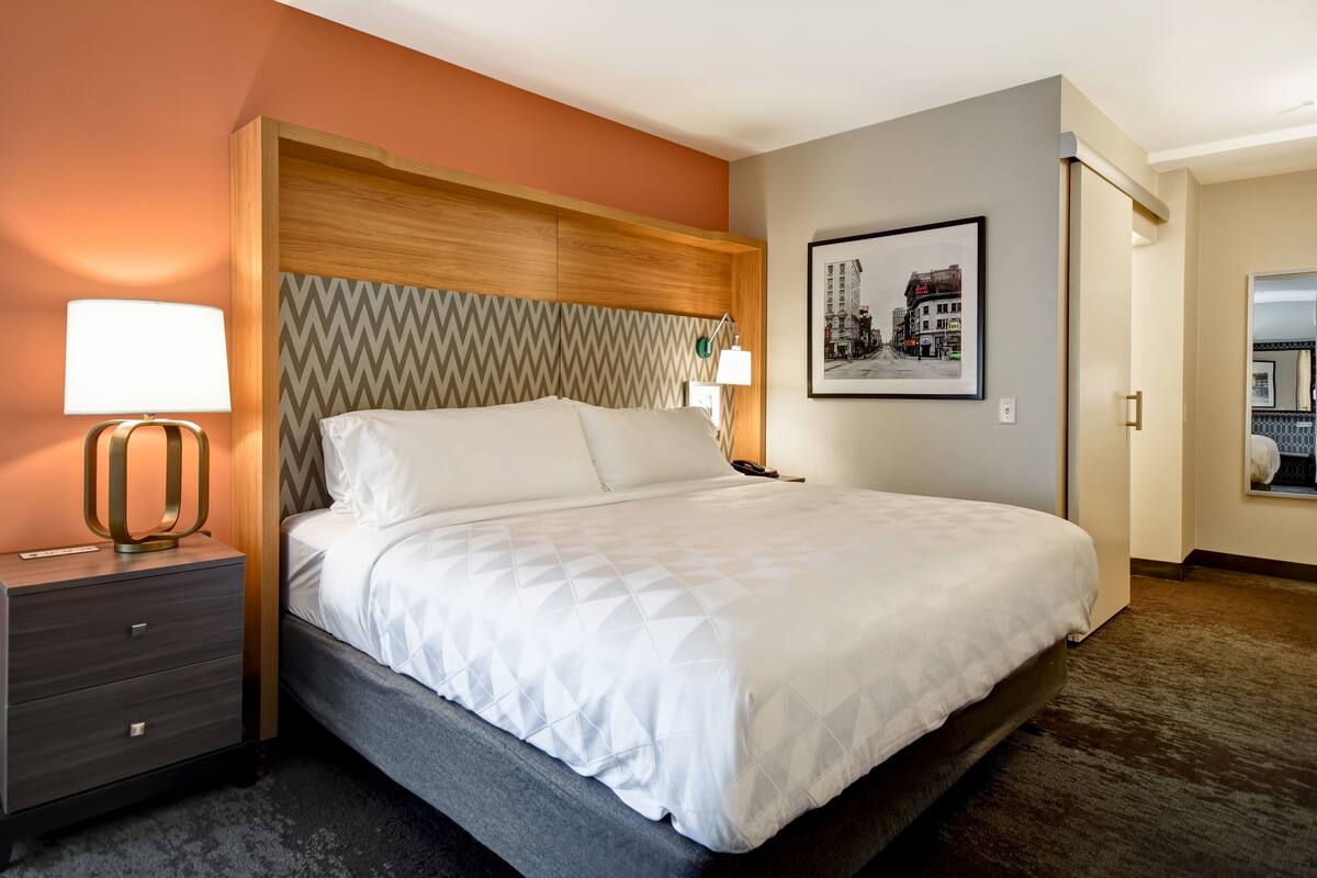 A hotel room with a bed, a nightstand, a lamp, and a framed picture on the wall.