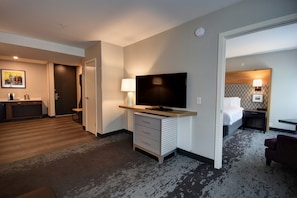 A hotel room with a flat-screen TV, a desk with a lamp, a bed with a headboard, and a chair.