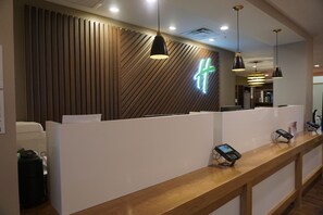 A reception area with a modern design, featuring a wooden panel wall, a neon sign, and a reception desk with a digital device.