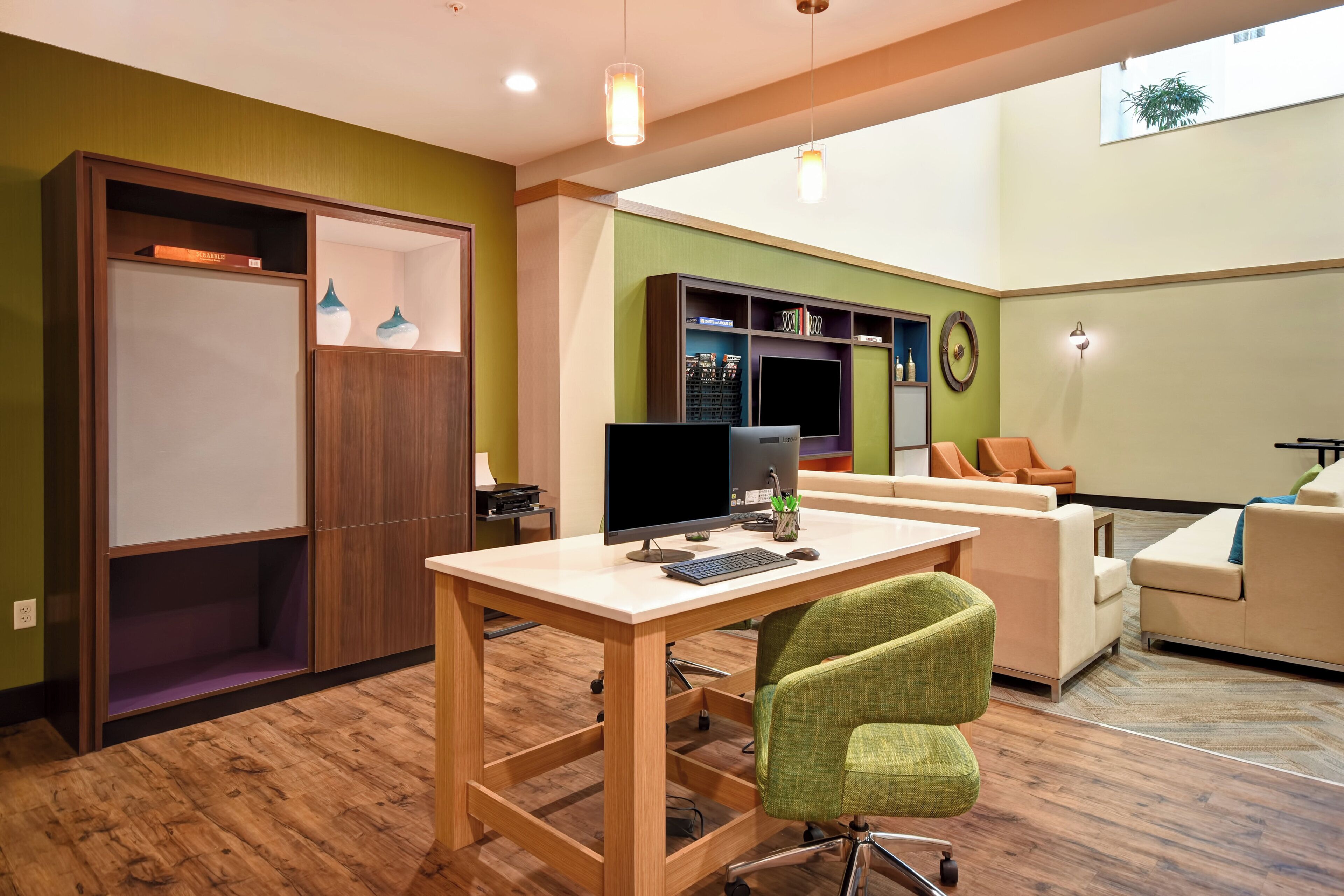 A modern living room with a wooden desk, a green chair, a sofa, and a bookshelf.
