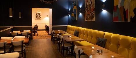 Un restaurante con una larga mesa de madera, un banco acolchado amarillo y una decoración moderna.