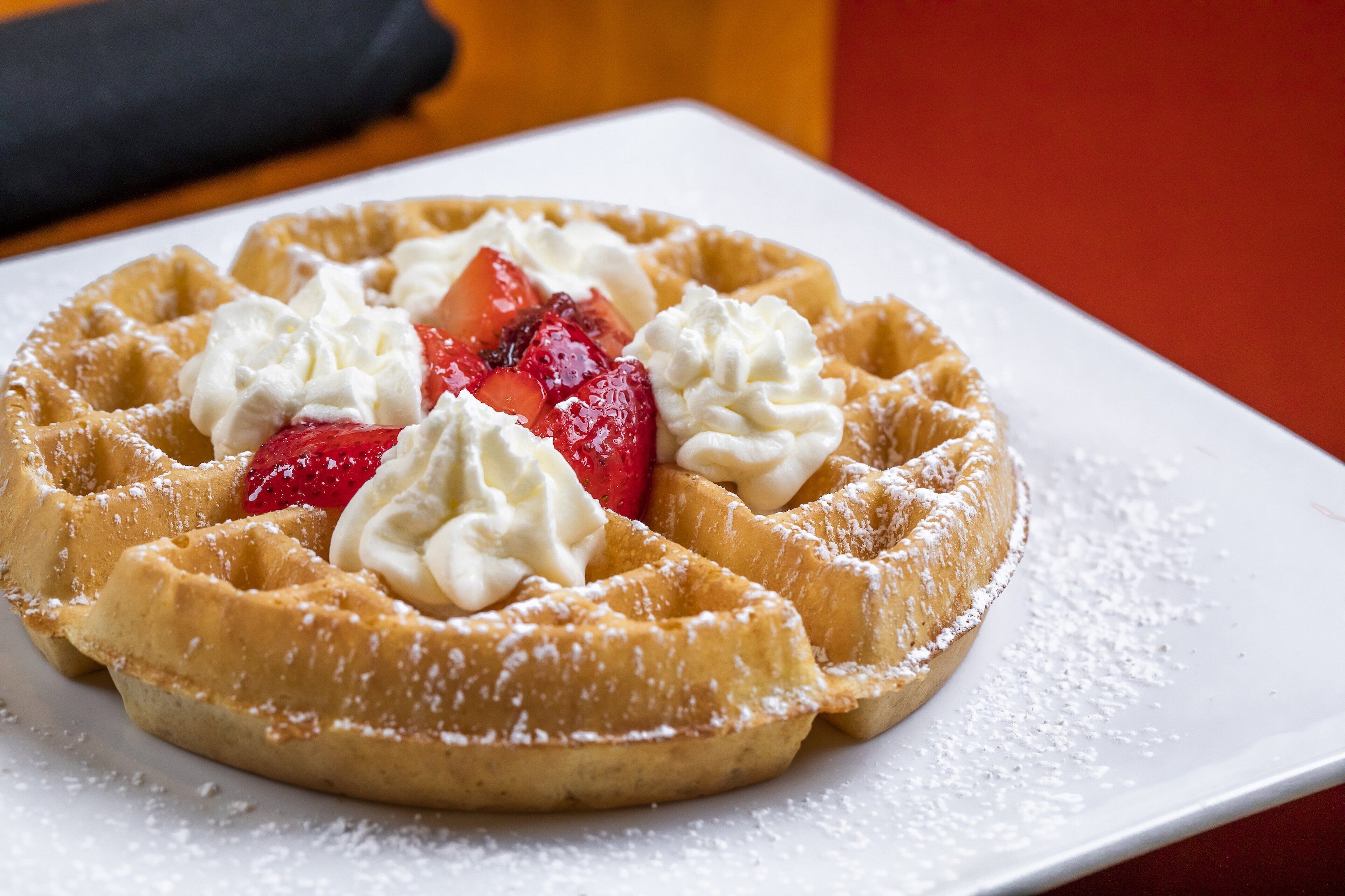 Un waffle con crema batida y fresas sobre un plato blanco.