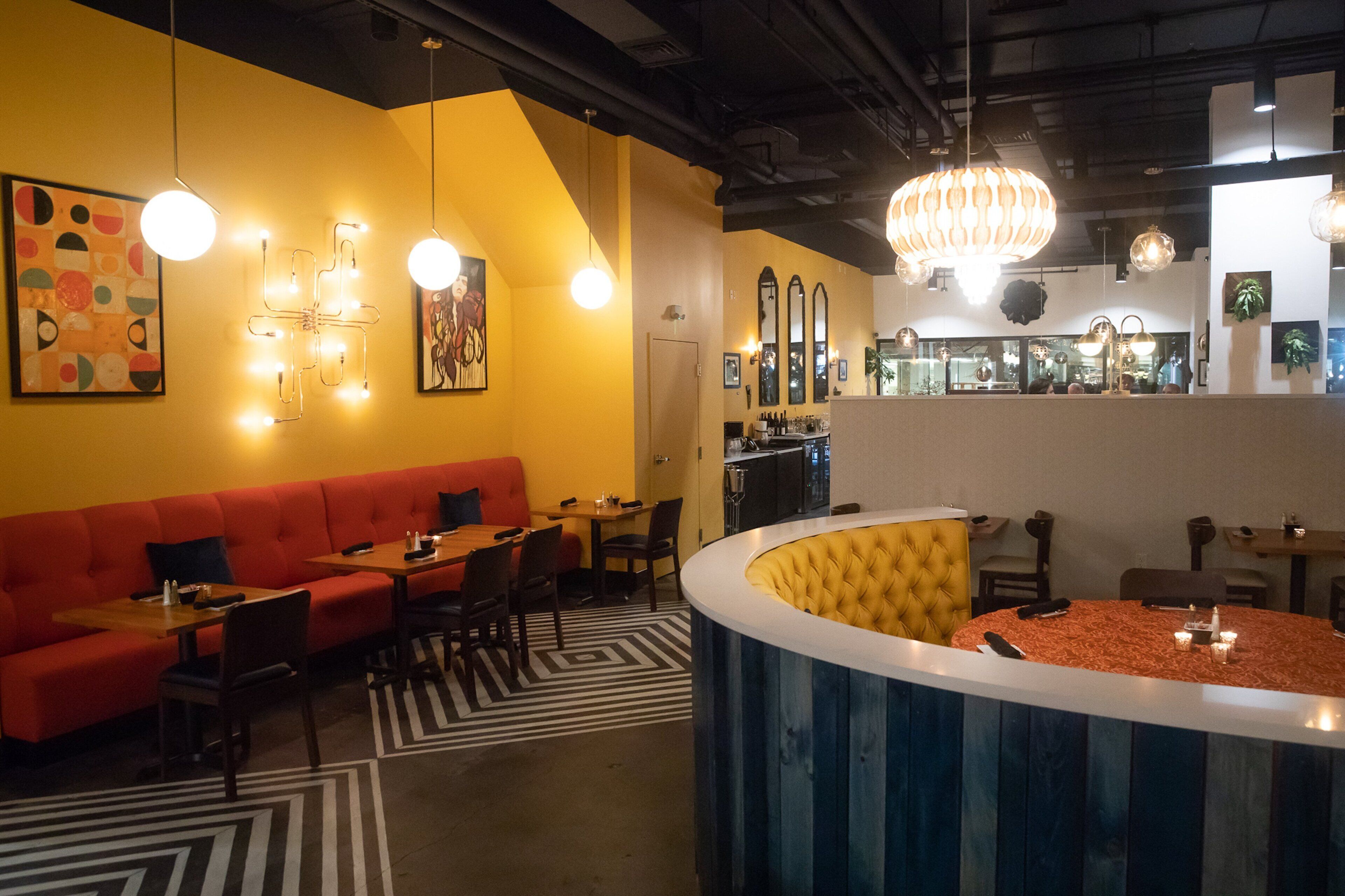 Un restaurante con un sofá rojo, mesas para comer y una zona de bar.