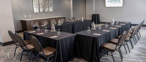 Un salón de conferencias con largas mesas, sillas y un cartel que dice 'The Imperial Event Center'.