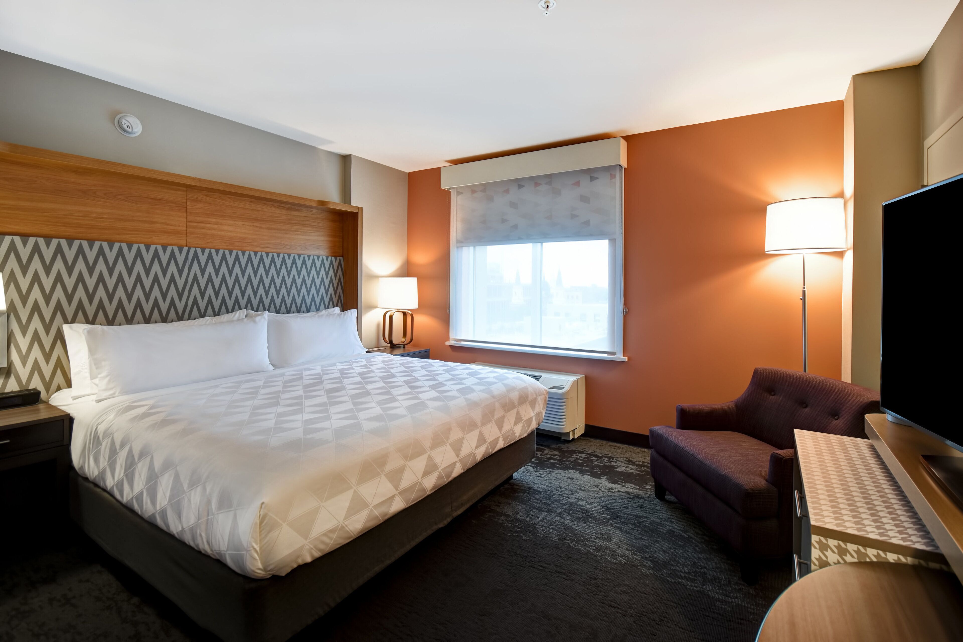 Quarto de hotel com uma cama grande, televisão, escrivaninha, cadeira e janela com vista.