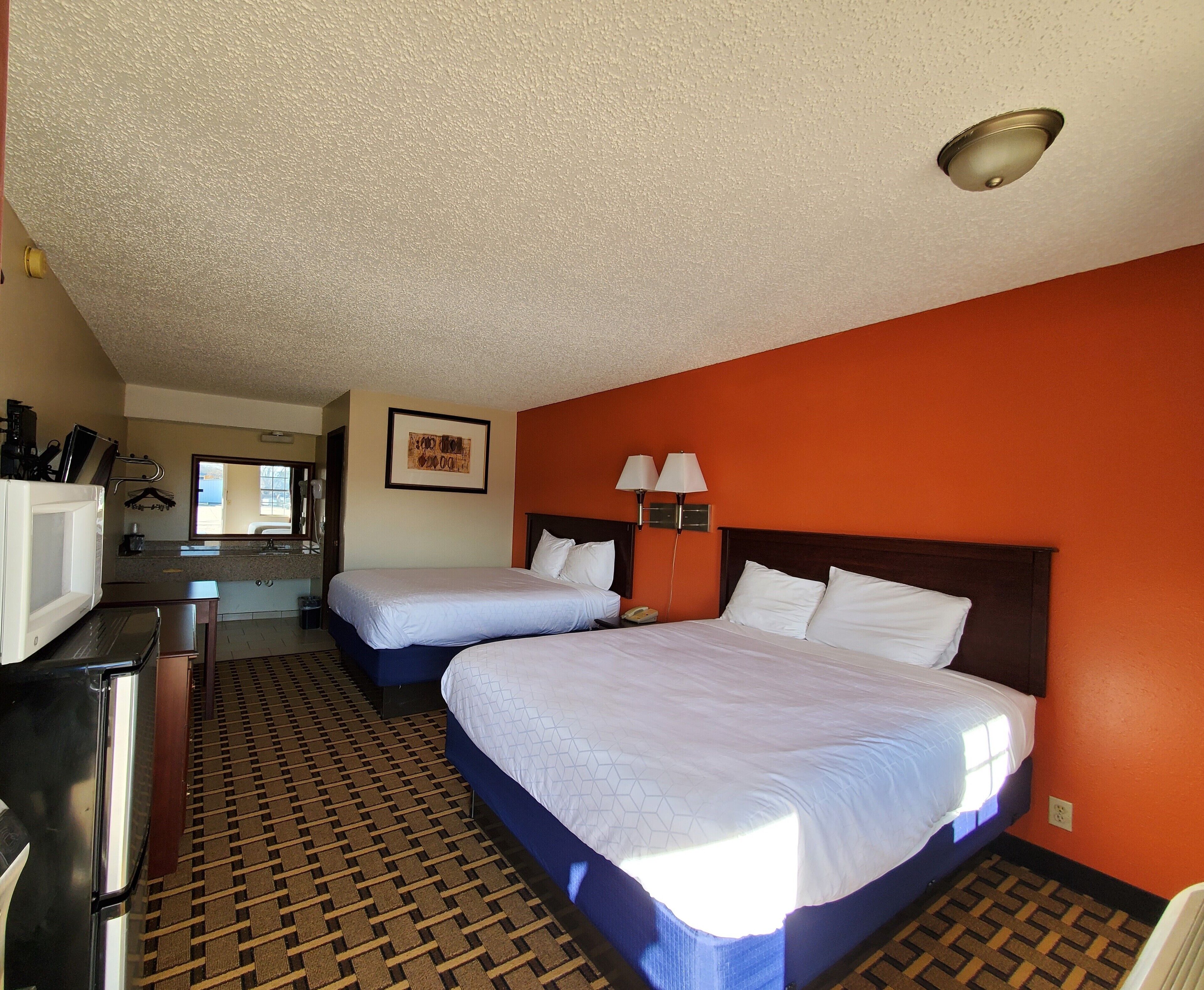 A hotel room with two beds, a desk, a microwave, a sink, and a mirror.