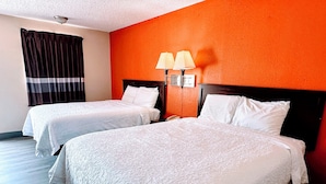 Habitación de hotel con dos camas, una mesita de noche, una lámpara y una pared naranja.
