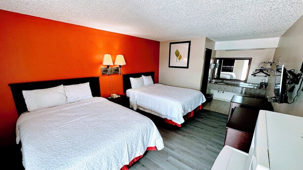 Habitación de hotel con dos camas, un escritorio, una silla, un espejo y un baño.