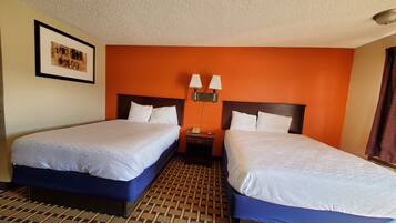 A hotel room with two beds, a patterned floor, a framed picture on the wall, and a nightstand with lamps.