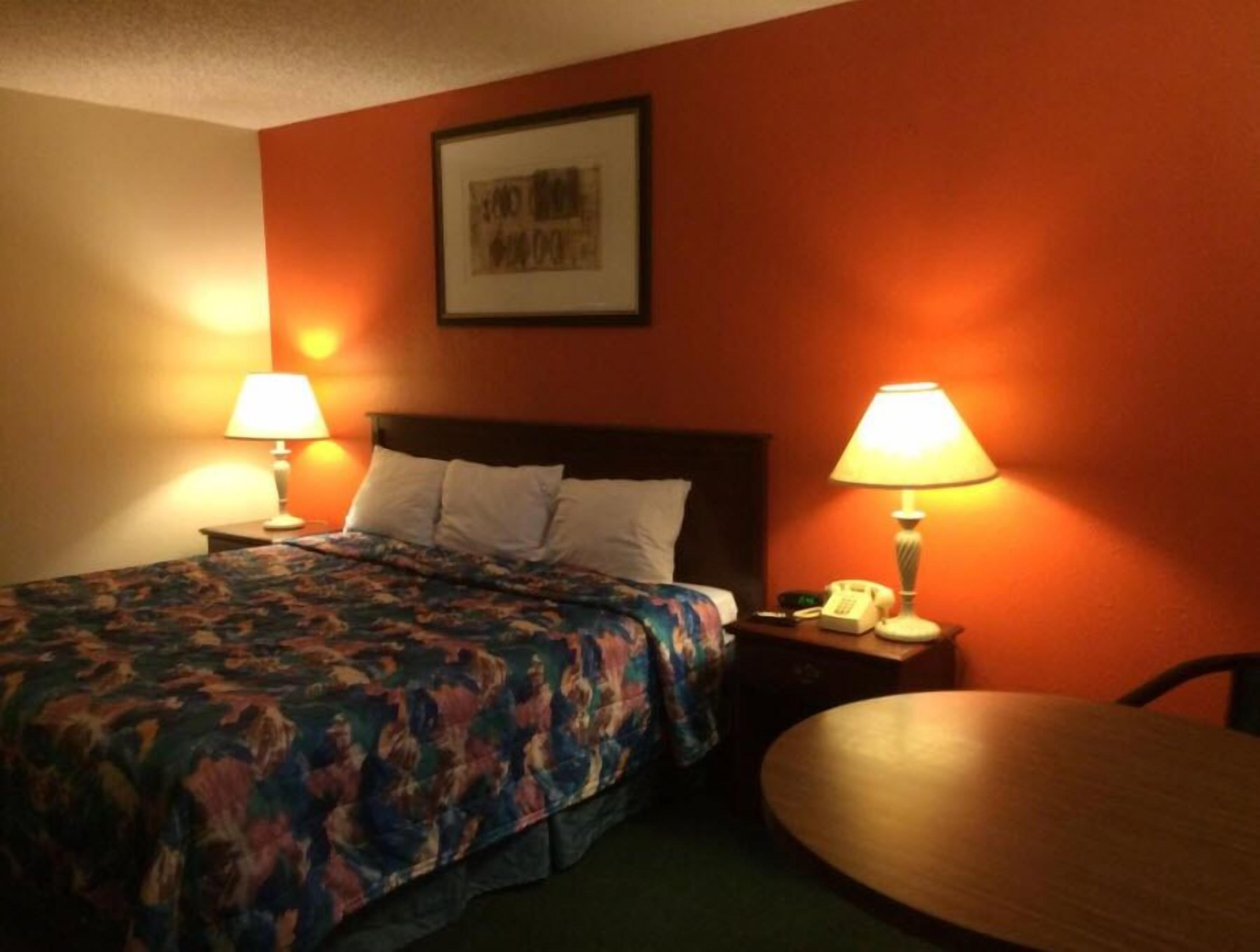 A hotel room with a bed, two bedside lamps, a telephone, and a round table.
