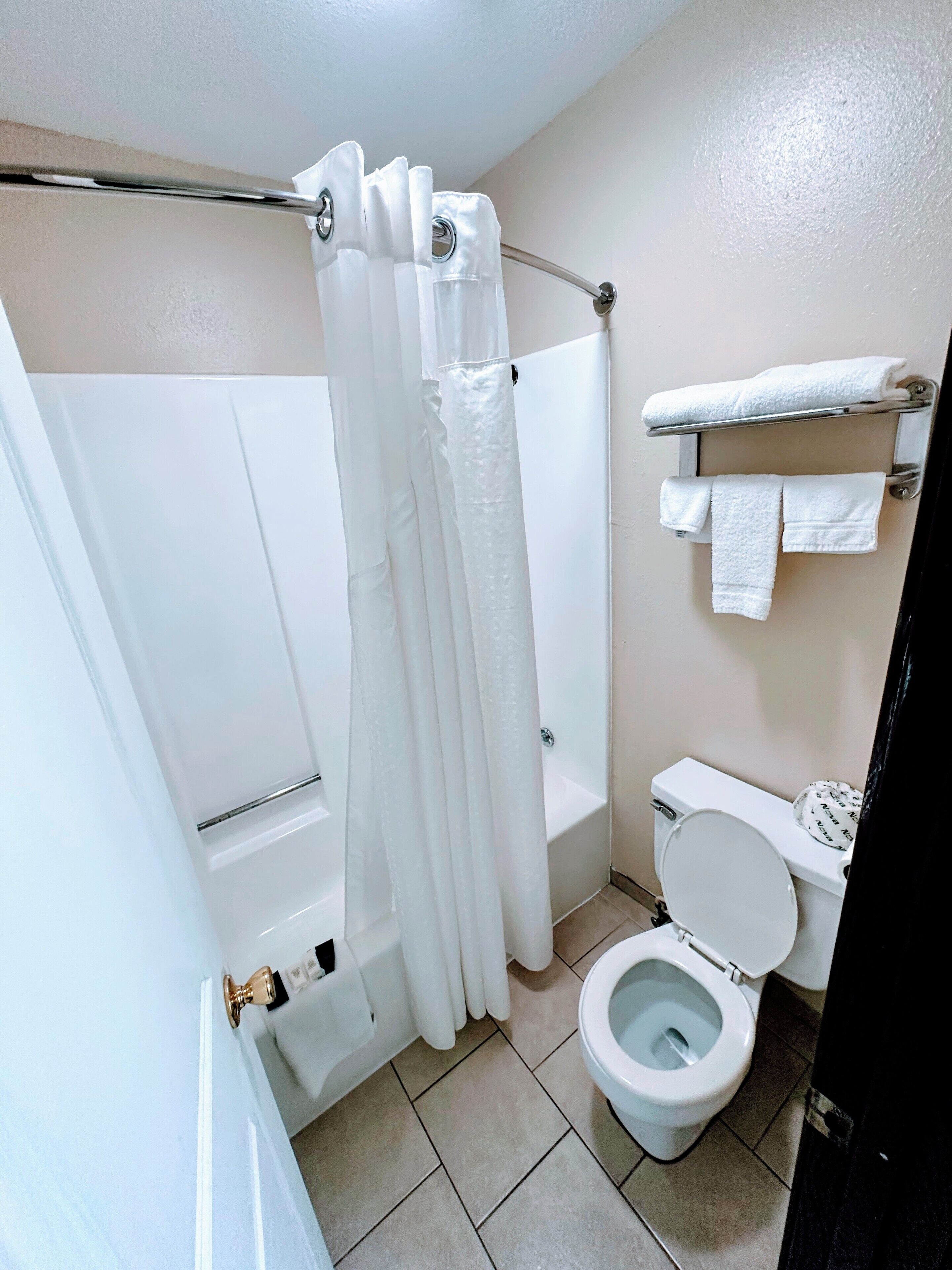 Een badkamer met douchegordijn, bad, toilet en een handdoekrek met handdoeken.