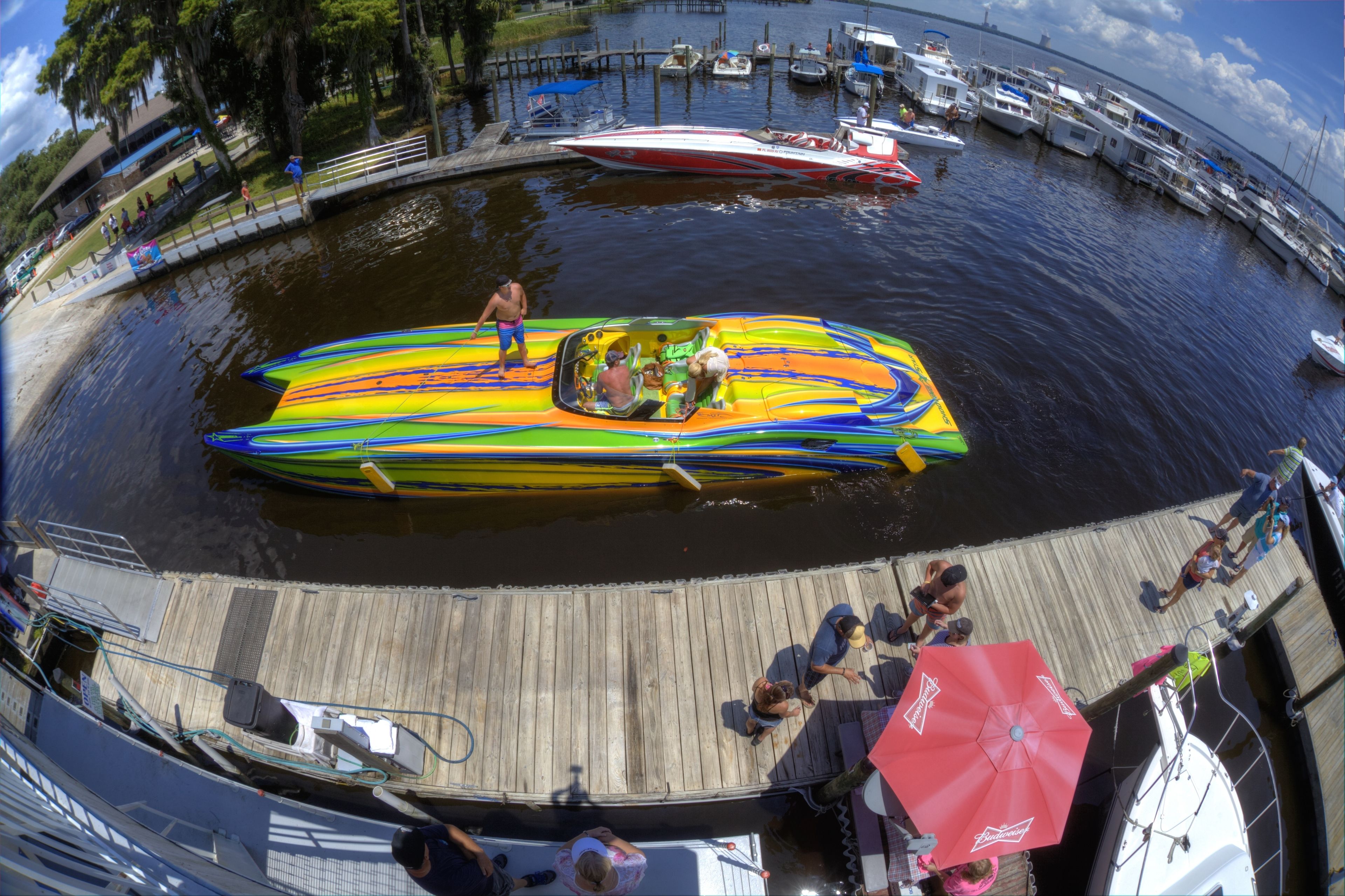 Un muelle con una colorida balsa inflable en el agua, rodeado de barcos y un embarcadero con gente.