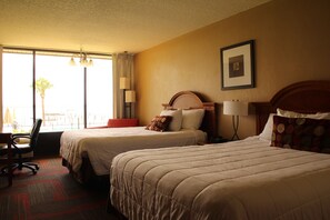 A hotel room with two beds, a desk, and a chair. There is a window with curtains, a lamp, and a framed picture on the wall. - Crystal Cove Hotel (Palatka)