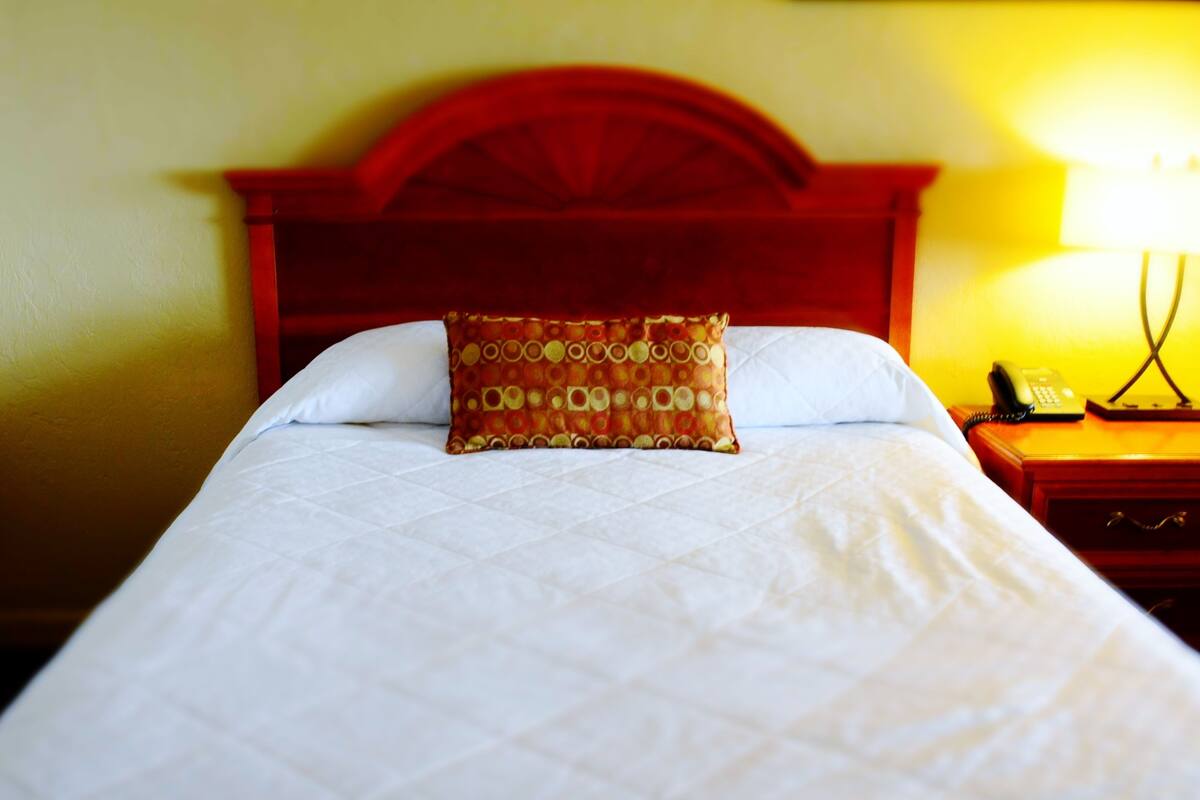 Una cama con un cojín estampado, cabecera de madera y una mesita de noche con lámpara.