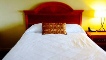 A bed with a patterned pillow, a wooden headboard, and a bedside table with a lamp.