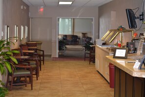 A hotel lobby with wooden chairs, a reception desk, and a television mounted on the wall. - Crystal Cove Hotel (Palatka)