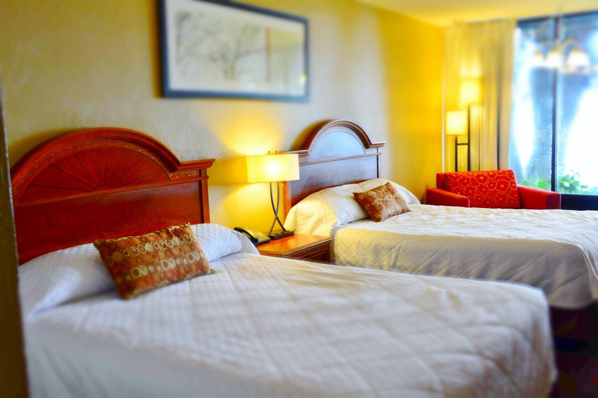 Habitación de hotel con dos camas, una silla roja y una lámpara.