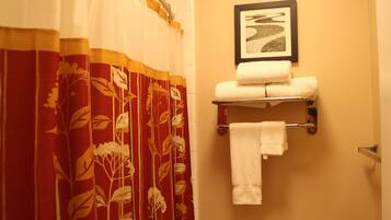 A bathroom with a shower curtain, a towel rack with two towels, and a framed picture on the wall.
