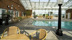 An indoor swimming pool area with wicker chairs and a glass-enclosed ceiling. - Carlisle Inn Sugarcreek (Sugarcreek)