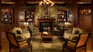 A traditional library with wooden bookshelves, two armchairs, a fireplace, and a chandelier. - Carlisle Inn Sugarcreek (Sugarcreek)
