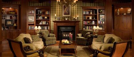 Une bibliothèque traditionnelle avec des étagères en bois, deux fauteuils, une cheminée et un lustre.