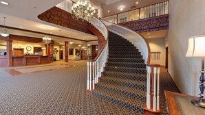 A grand lobby with a curved staircase, a reception desk, and a chandelier. - Carlisle Inn Sugarcreek (Sugarcreek)