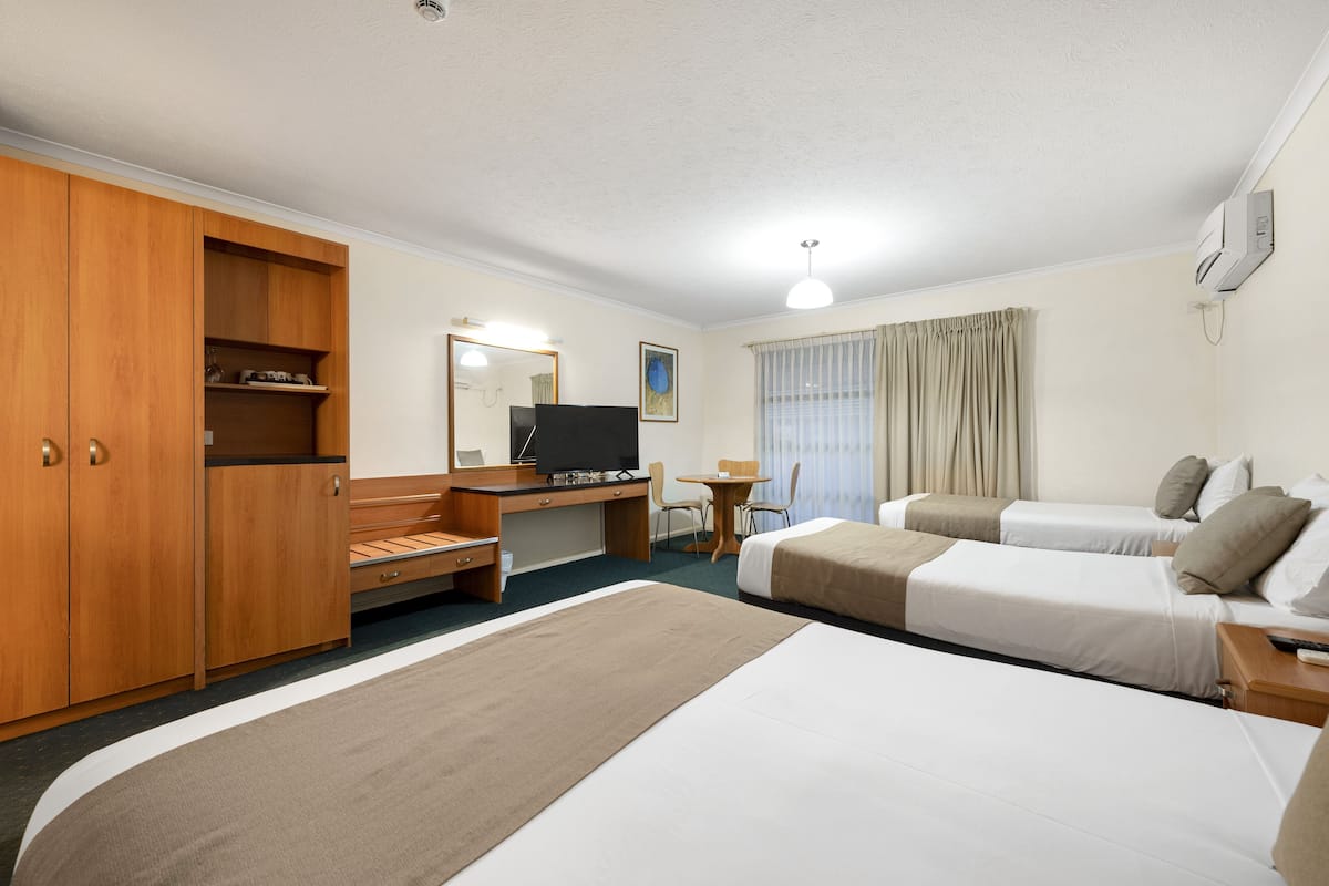 A hotel room with a large bed, a desk with a television, a chair, and a small table.