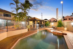 A swimming pool with a brick deck, surrounded by a fence and palm trees. - Pegasus Motor Inn and Serviced Apartments (Hamilton)