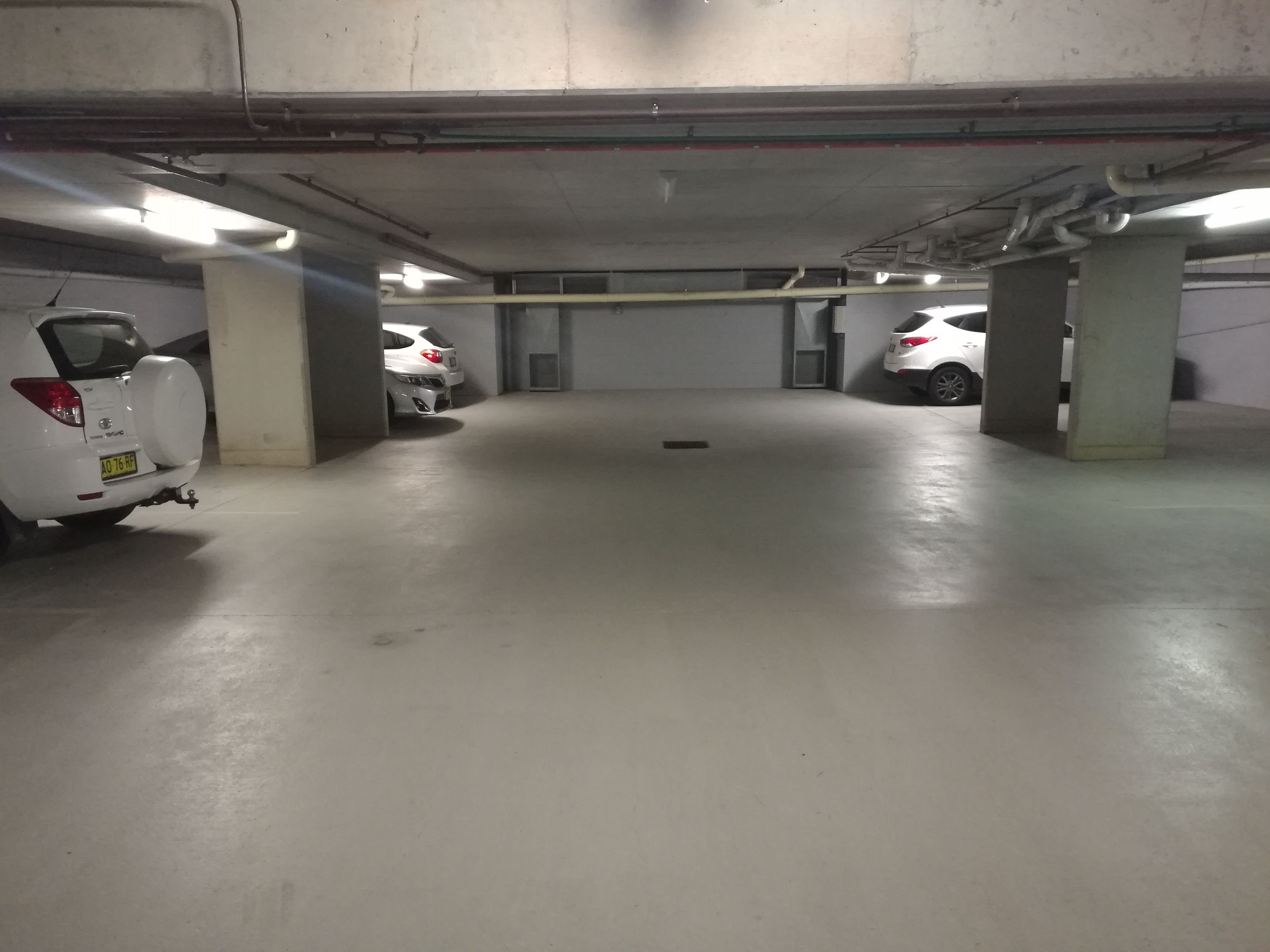 Un aparcamiento con pilares de hormigón, iluminación fluorescente y tres coches blancos estacionados.