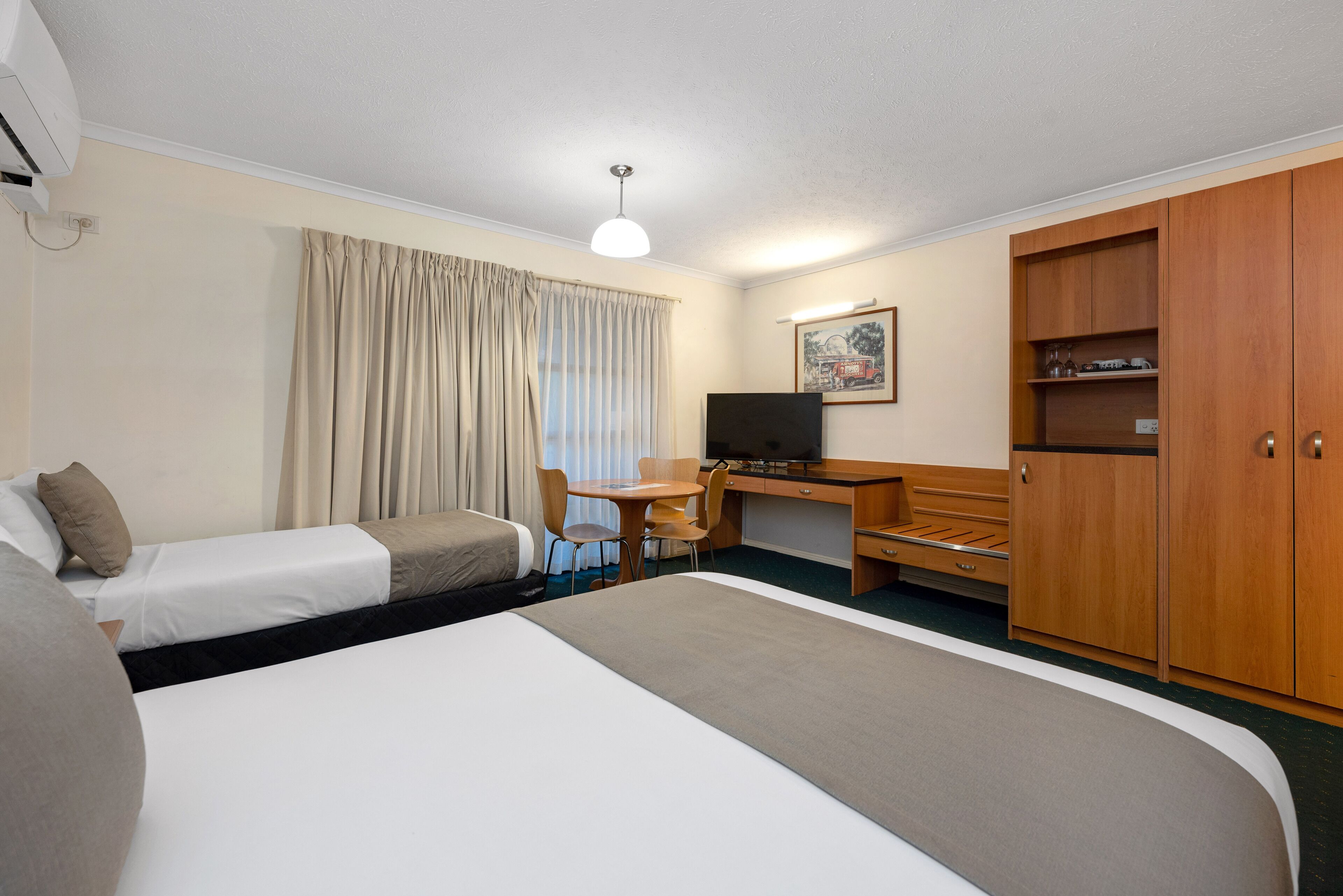 A hotel room with two beds, a desk, a chair, a television, and a wardrobe.
