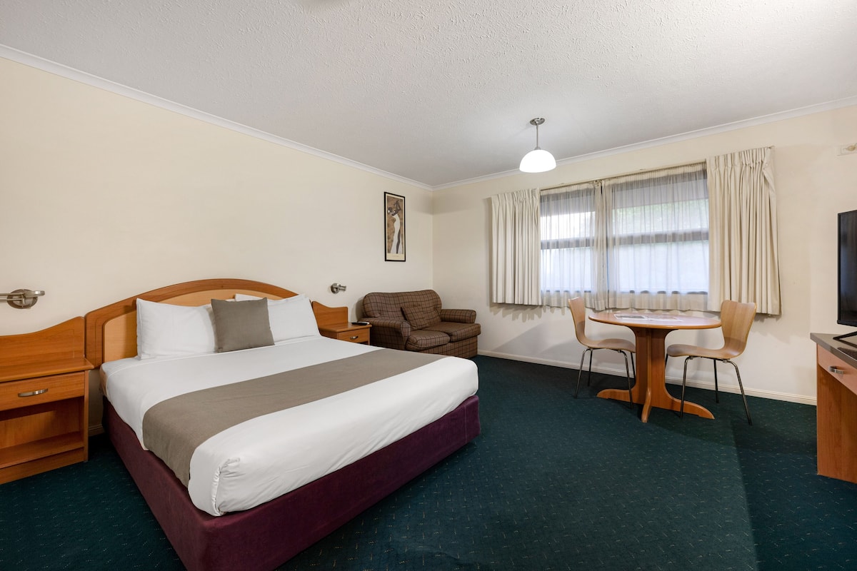 A hotel room with a bed, a desk, a chair, a sofa, and a television.