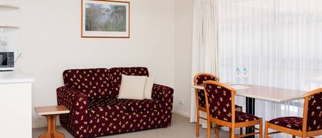 A compact living space with a sofa, two chairs, a small table, and a microwave.