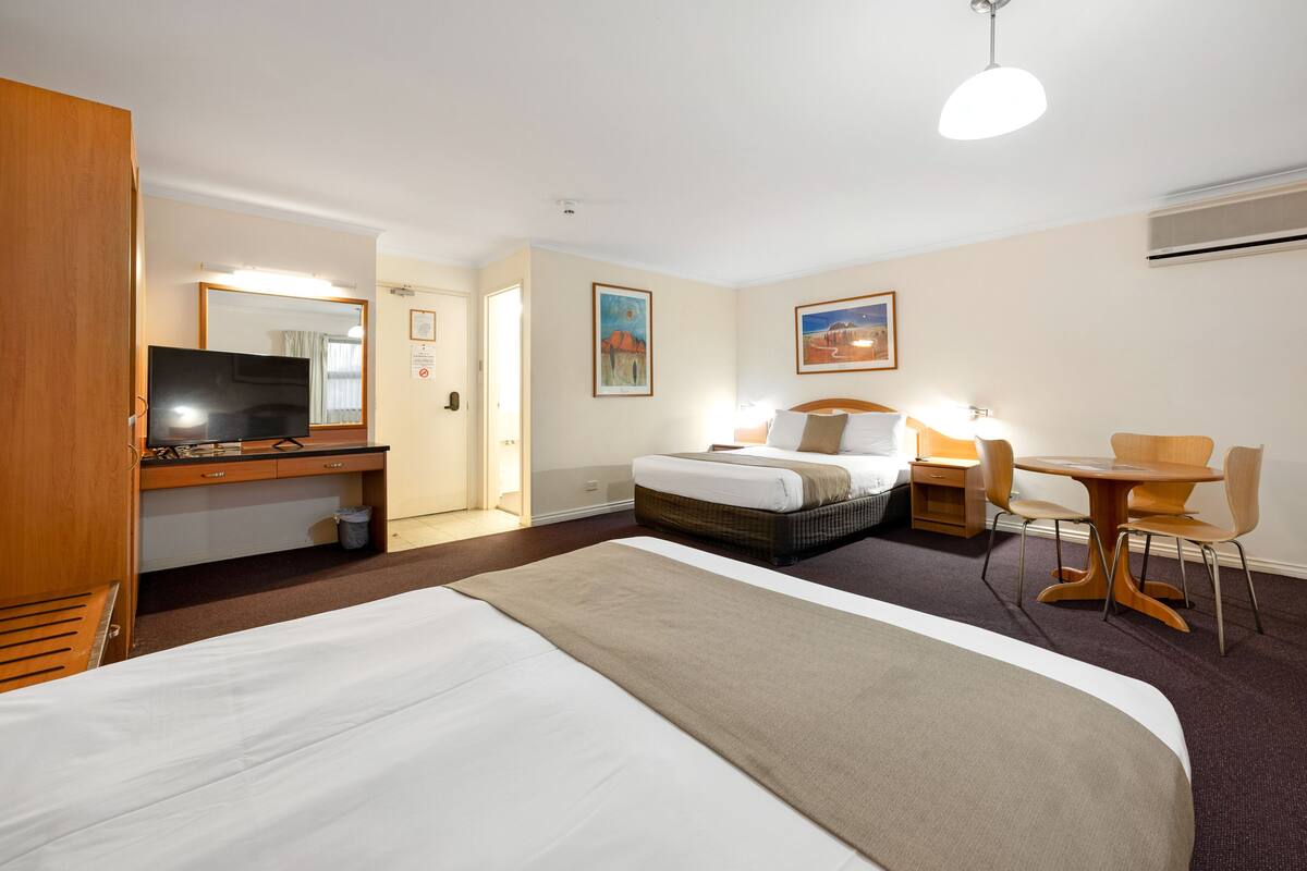 A hotel room with a large bed, a desk with a computer, a chair, a small table, and a television.