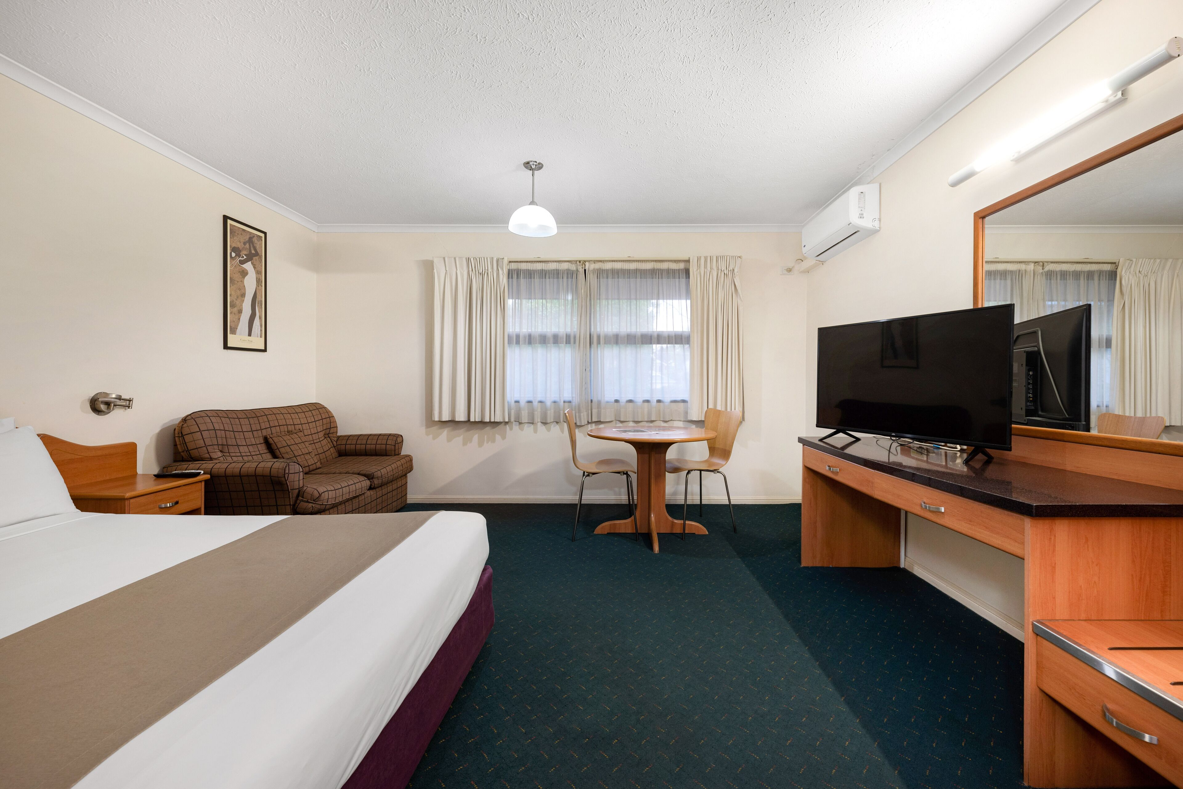 Habitación de hotel con cama, escritorio con televisor, silla, mesa y ventana con cortinas.