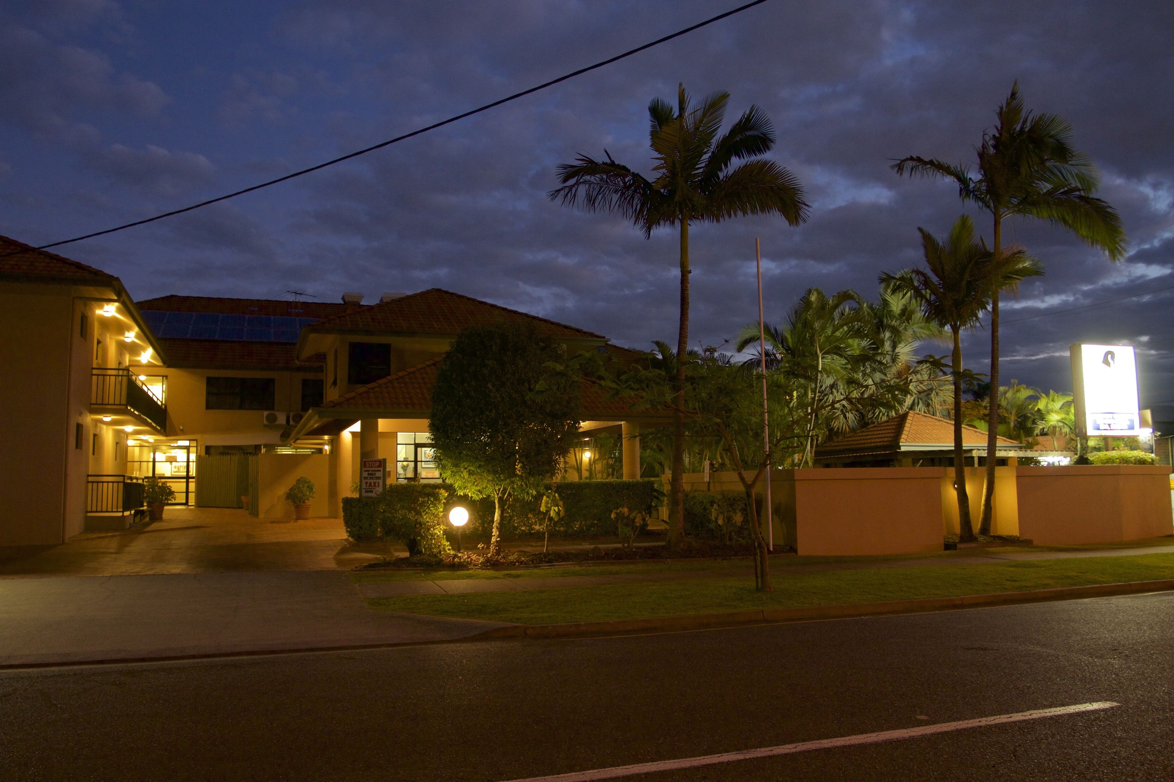 Un hotel con una entrada bien iluminada, palmeras y cielo despejado.