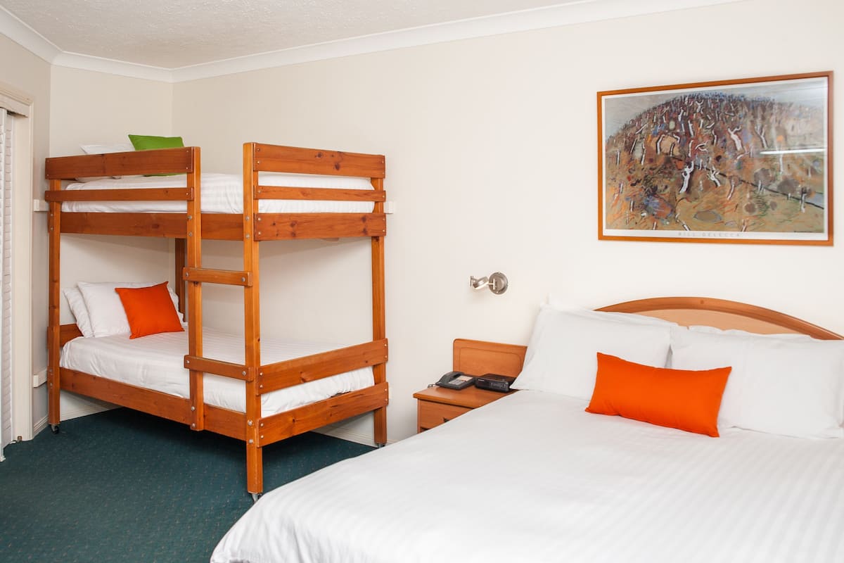 A hotel room with a bunk bed, a single bed, and a painting on the wall.