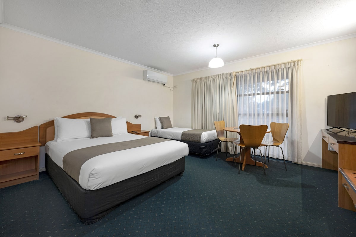 A hotel room with two beds, a desk, a chair, a TV, and an air conditioning unit.