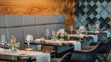 Ein Restaurant mit modernem Interieur, das Ledersitzbänke und eine Wand mit Muster bietet. Die Tische sind mit Weingläsern, Besteck und dekorativen Elementen gedeckt.