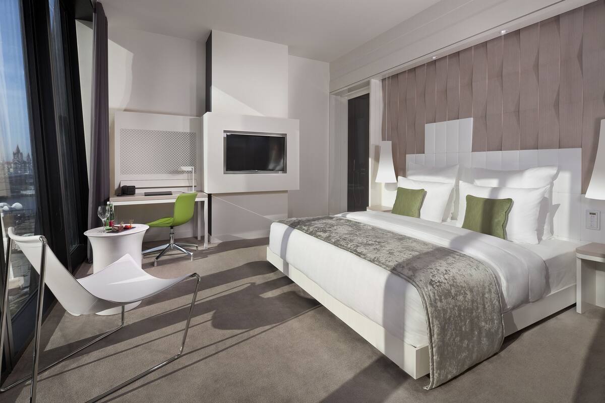 A modern hotel room with a large bed, a desk, a chair, and a TV mounted on the wall.