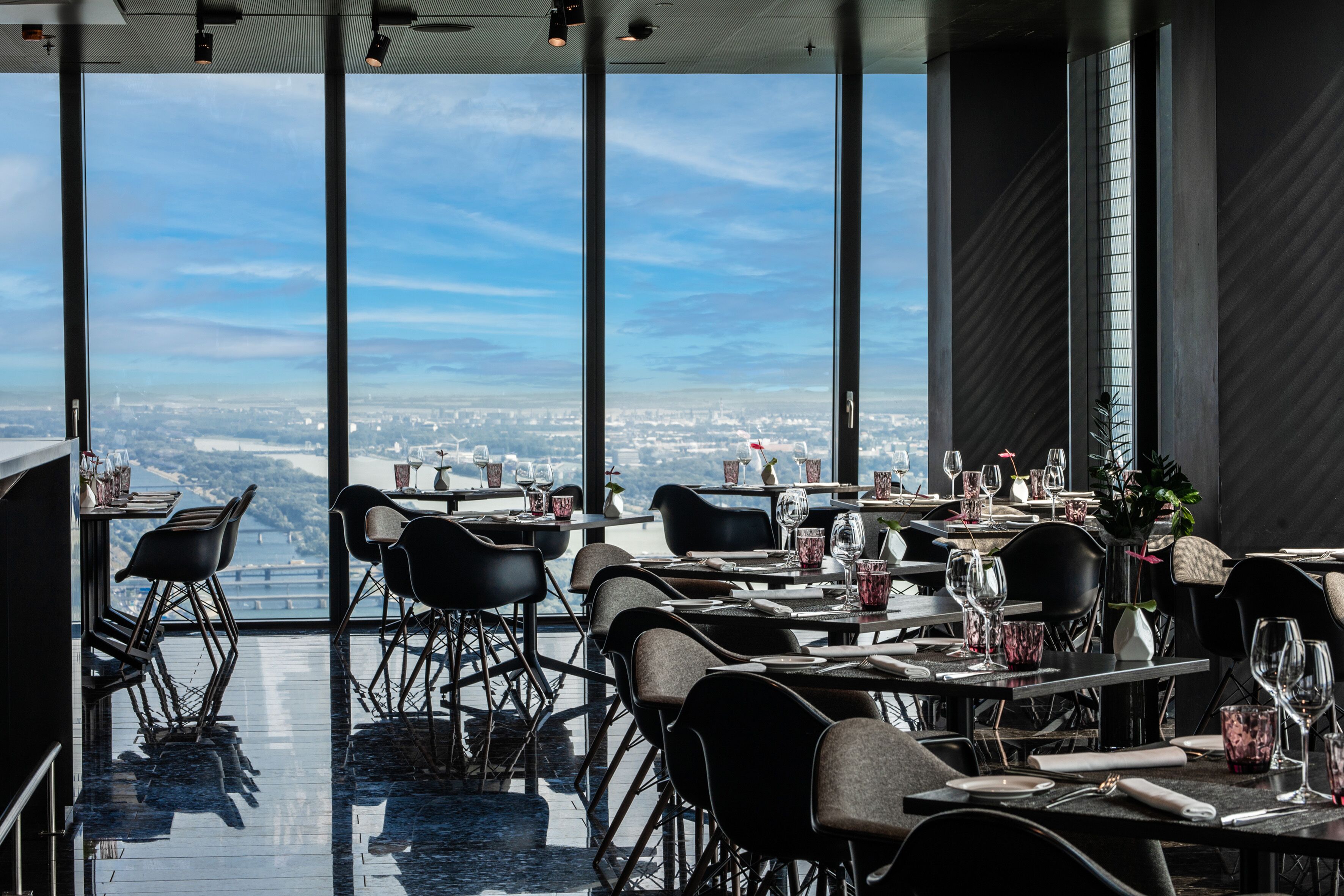 A restaurant with high tables and chairs, large windows offering a city view.