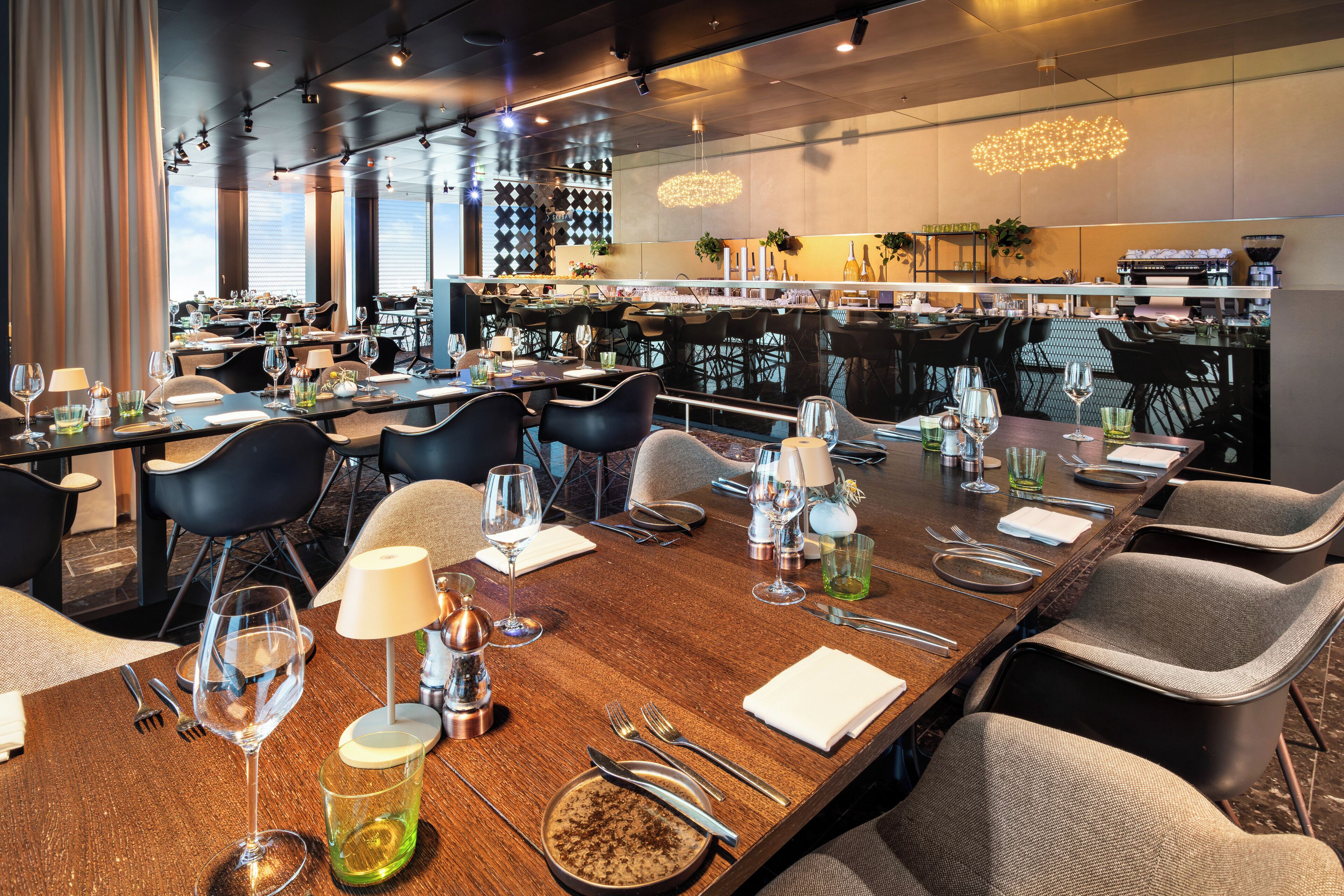 A modern restaurant with multiple dining tables, black chairs, and a bar area.