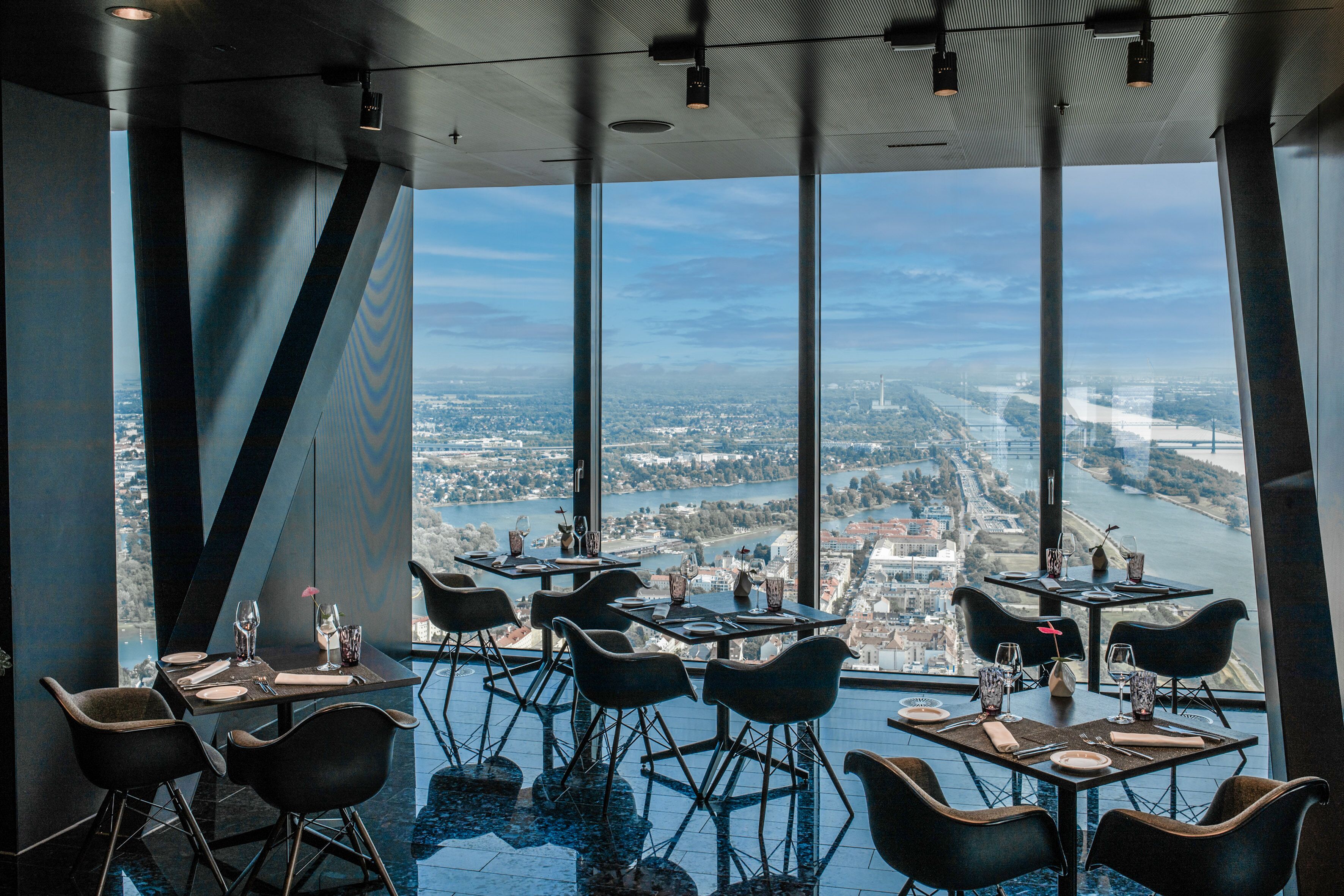 En restaurant med borde, stole, store vinduer og udsigt over by og flod.