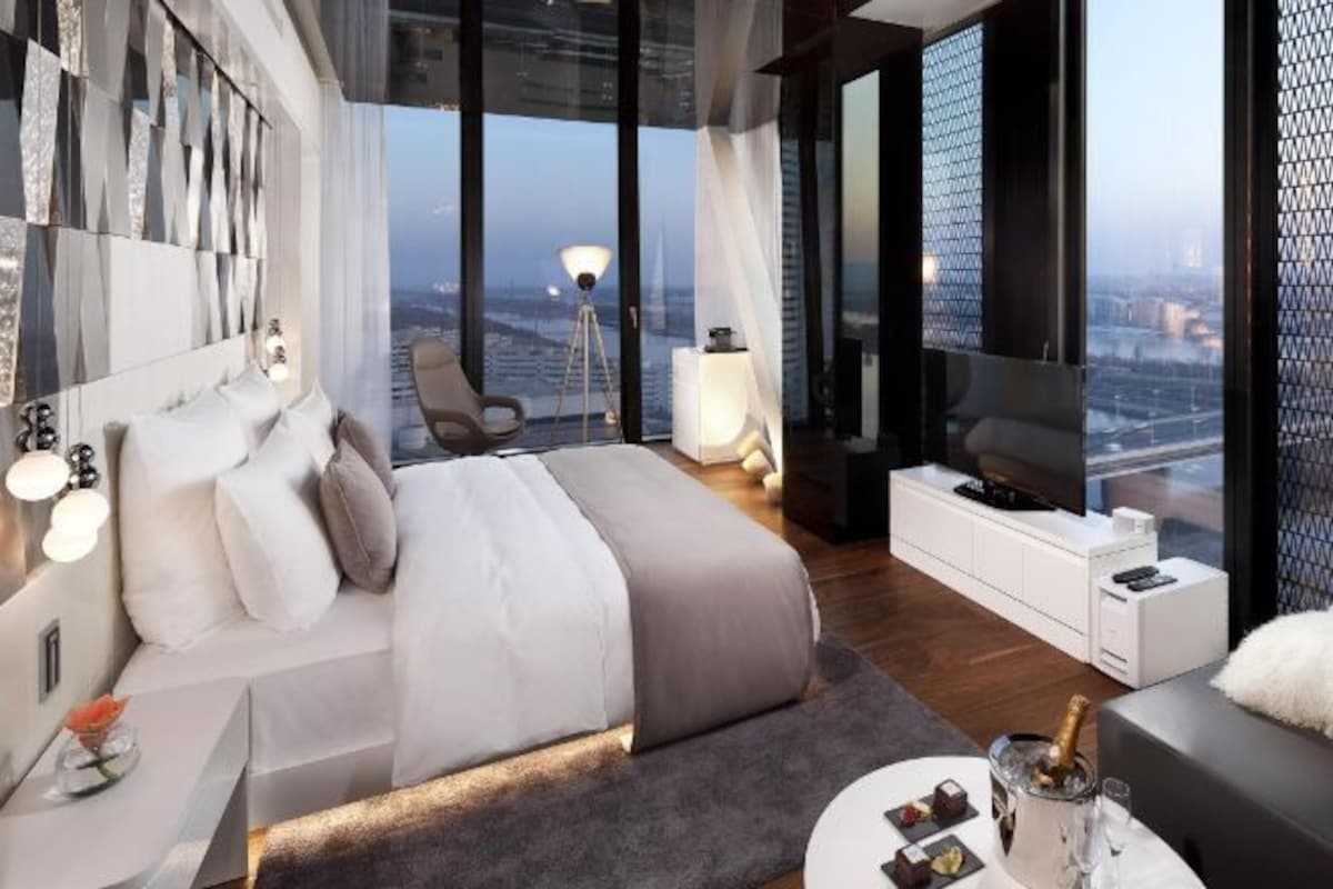 Une chambre moderne dot ée d’un grand lit, de tables de chevet, d’un coin salon et offrant une vue sur la ville.