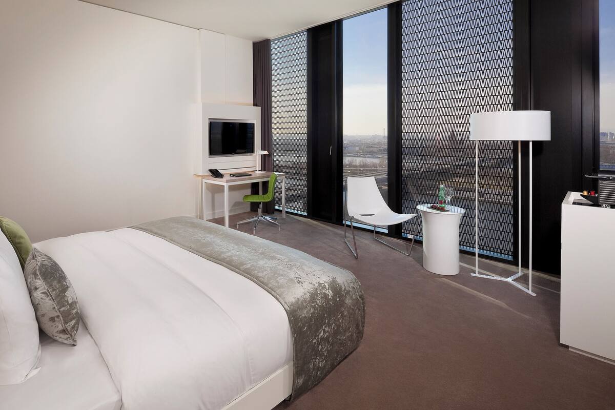 A modern hotel room with a large bed, a desk with a computer, a chair, and a TV.