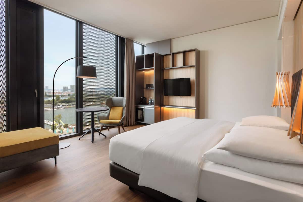 A modern hotel room with a large bed, a desk, a chair, and a TV mounted on the wall.