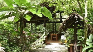 A covered outdoor area with a wooden structure, surrounded by lush greenery and various plants. - Arenal Oasis (La Fortuna)